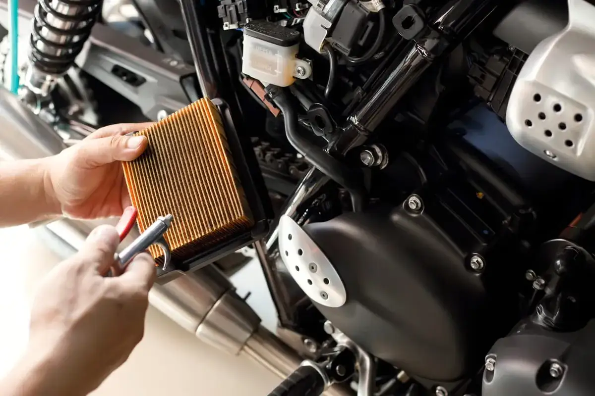Mani che puliscono un filtro dell'aria per moto con aria compressa. Questo componente è fondamentale per garantire che il motore riceva aria pulita, ottimizzando le prestazioni e la durata.