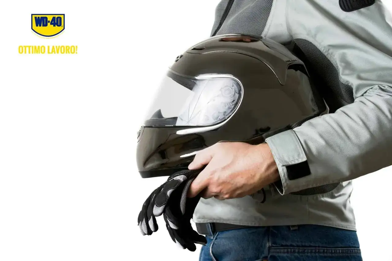 Un motociclista tiene in mano un casco nero e guanti. Ricorda: il casco non deve essere pulito con benzina.
