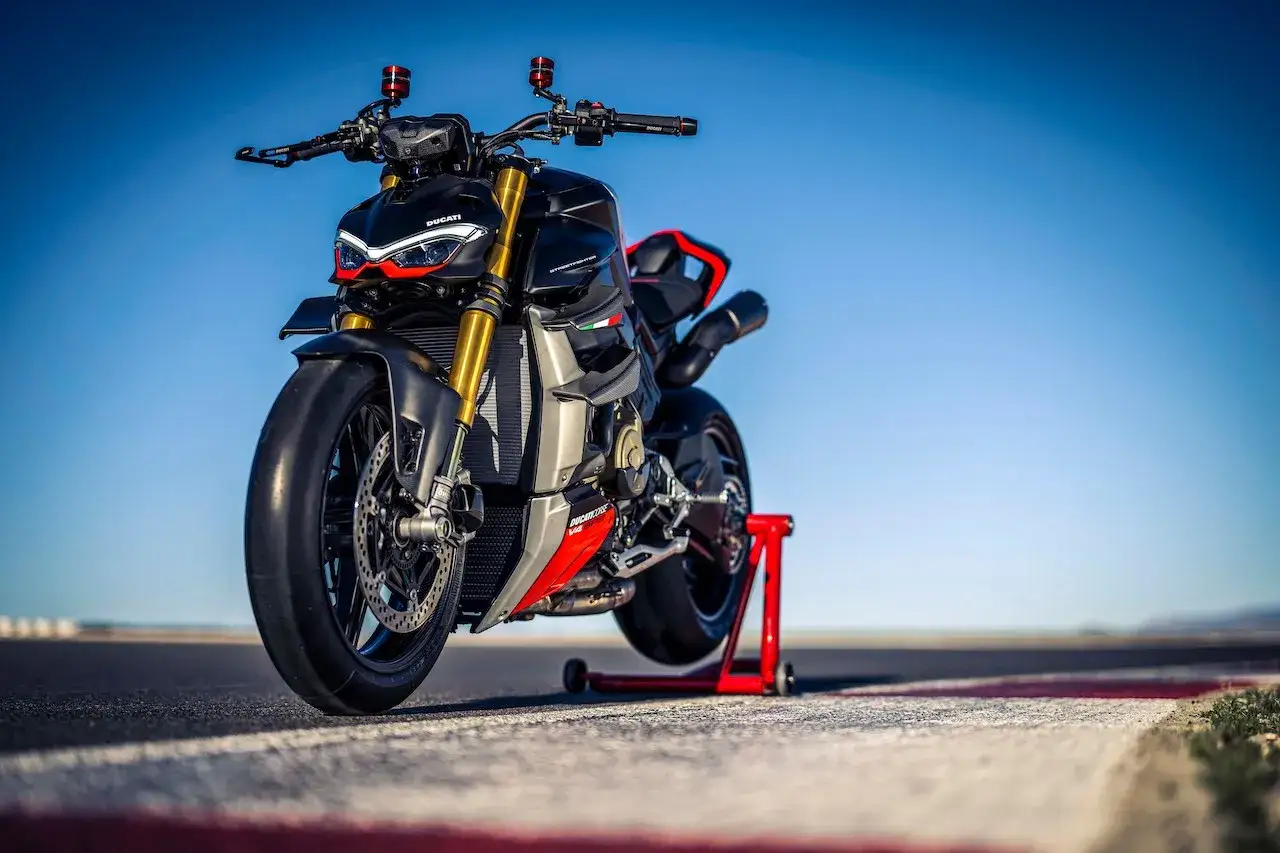 Ducati Streetfighter SP, nera e rossa, su cavalletto rosso, su asfalto con linee bianche e rosse, sotto un cielo azzurro.