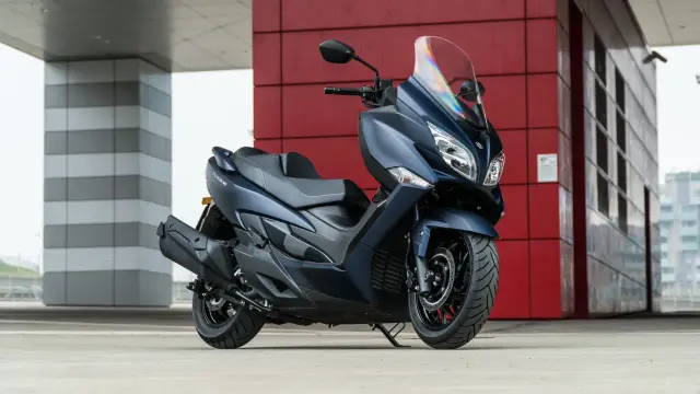 Un elegante scooter blu scuro, una perfetta moto da città, parcheggiato davanti a un edificio moderno con pareti rosse e grigie.