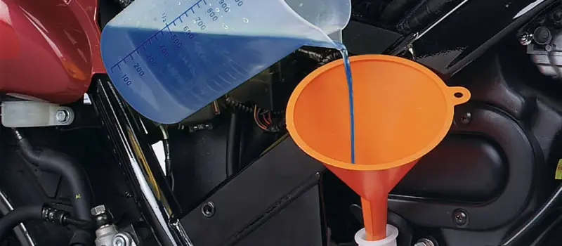 Versando liquido refrigerante blu in un imbuto arancione per diluirlo.