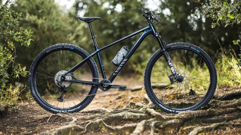 Muscle bike Canyon blu scuro su sentiero sterrato con radici affioranti.