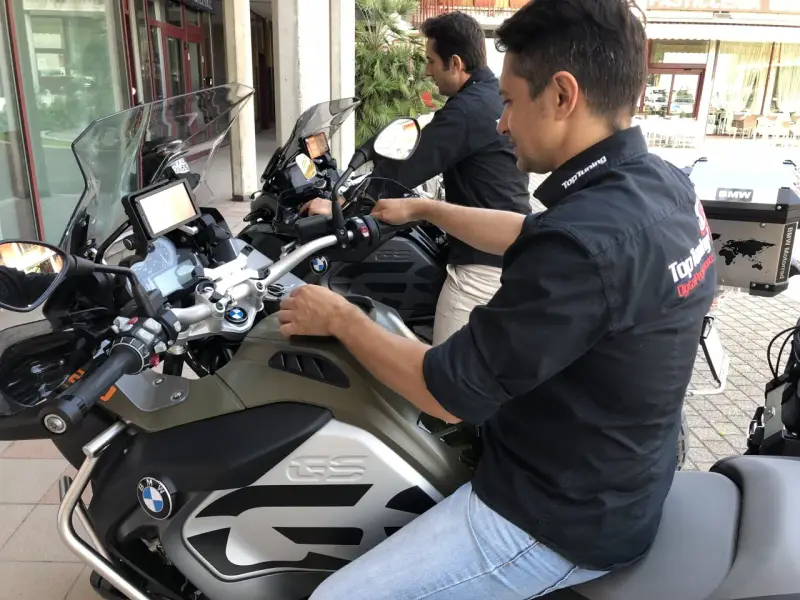 Due uomini in moto BMW, forse in fase di rodaggio, con abbigliamento tecnico. Il significato del rodaggio è fondamentale per la longevità del mezzo.