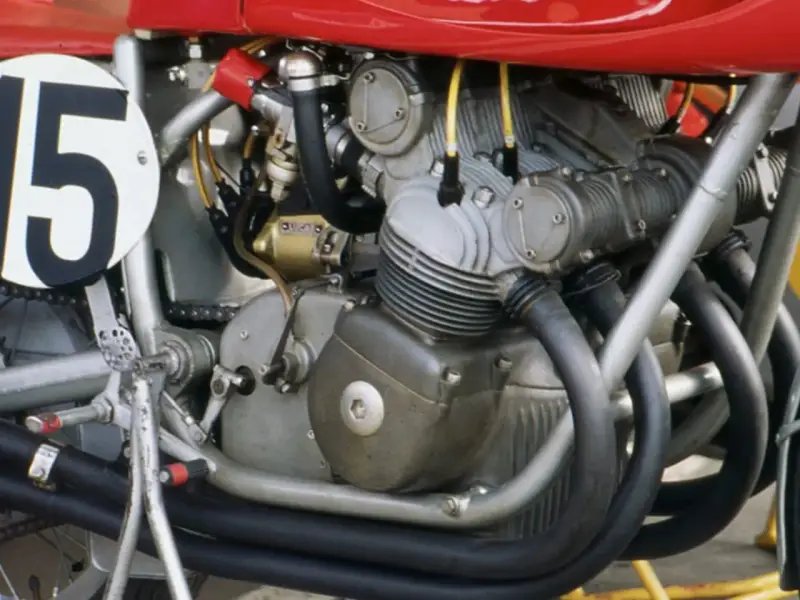 Dettaglio del motore di una moto da corsa, con il numero 15 su un cerchio bianco. Il motore è un complesso di tubi e metallo, pronto a ruggire.